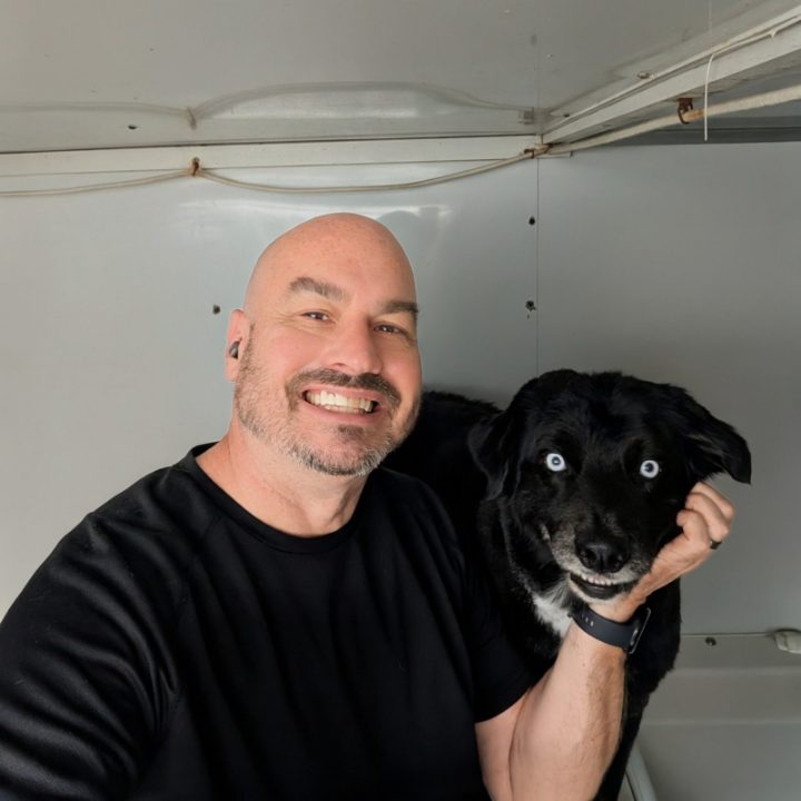 Paul Nickerson smiling next to Kai, an Australian Shepherd